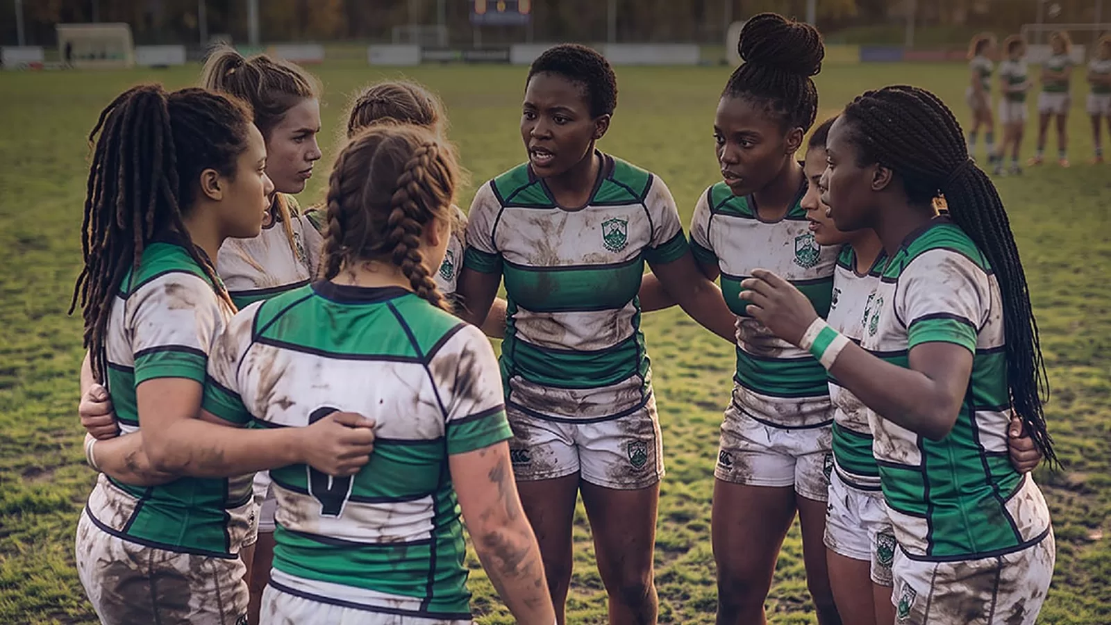 Girls rugby players in green and white jerseys huddle on the field during the Green Elly Rugby Festival